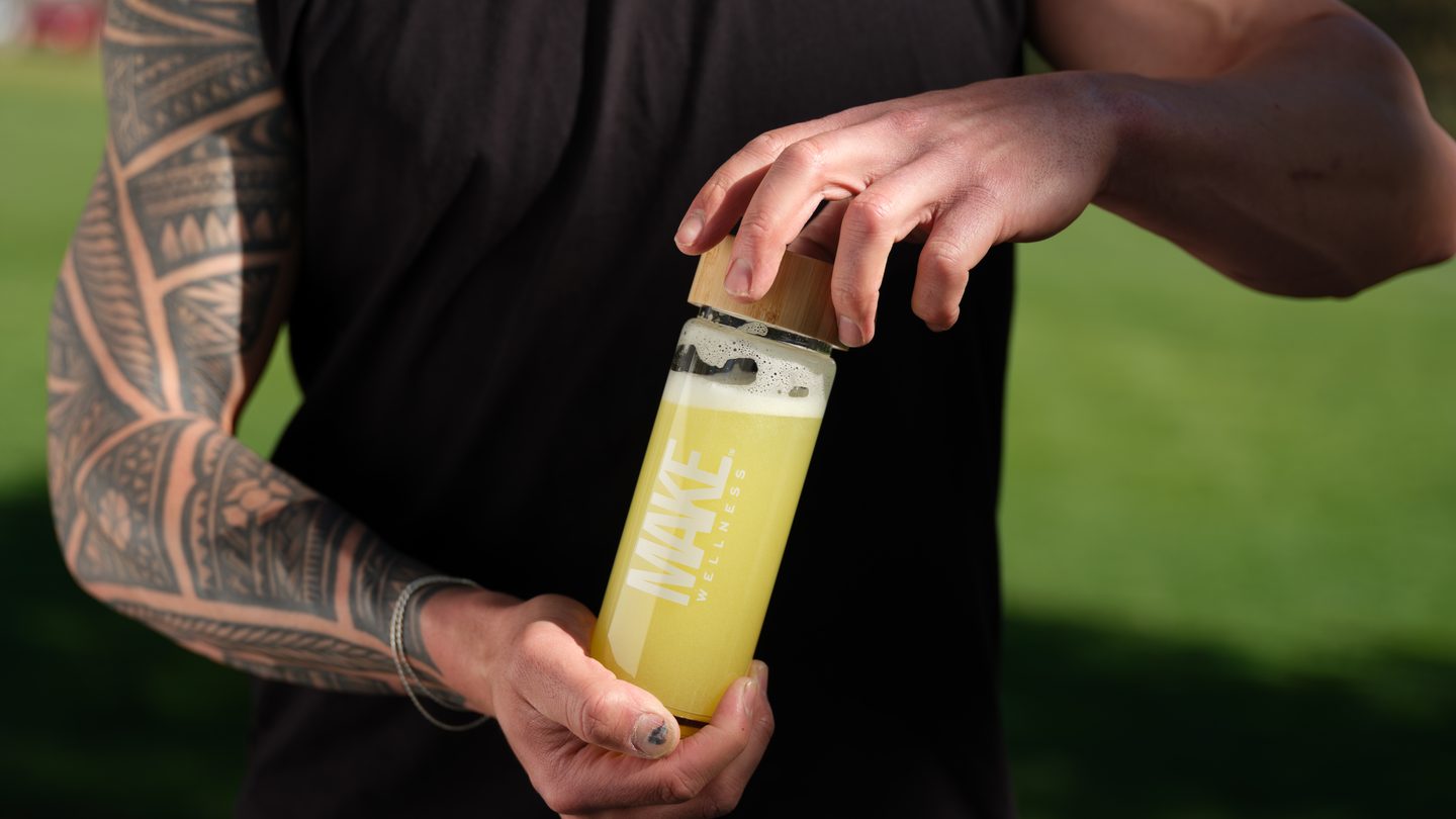 A man mixing a MAKE Wellness peptide drink outdoors after training